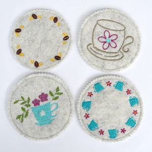 Peut inclure: Quatre dessous-de-verre ronds en feutre avec des motifs brodés. Un dessous-de-verre représente une tasse à café avec une fleur, un autre une tasse à café avec des feuilles et des fleurs, un autre un cercle de tasses à café et le dernier un cercle de grains de café.