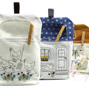Peut inclure: Trois pochettes en tissu avec des motifs variés. L'une représente des poulets et une fourche, une autre une maison et la troisième un motif floral. Chaque pochette a une pince à linge en bois et une poignée en tissu.