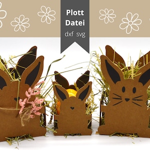 Könnte beinhalten: Drei braune Papphasen-Körbe mit schwarzen Ohren und Gesichtern. Die Körbe sind mit getrocknetem Gras gefüllt und der größte Korb hat eine kleine Blumenverzierung.