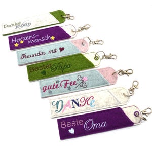 May include: Seven felt keychains with different embroidered designs and colors. The designs include "Danke sehr", "Herzens-mensch", "Freundin mit", "Bester Papa", "gute Fee", "DANKE", and "Beste Oma".