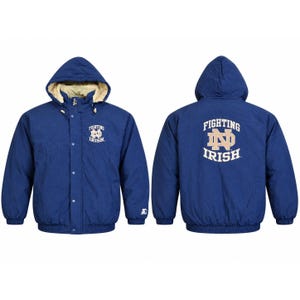 Puede incluir: Una chaqueta azul marino con capucha y forro color crema, con cierre de cremallera y botones a presión. La parte delantera muestra el logotipo de Notre Dame Fighting Irish, mientras que la espalda presenta el mismo logo en mayor tamaño.