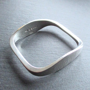 May include: A silver square-shaped bangle bracelet with a slightly curved design. The bracelet is marked with the text "925 STERLING".