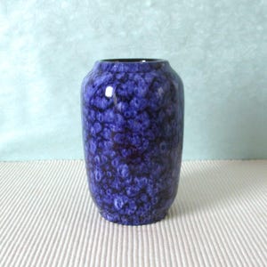 Può includere: Un vaso di ceramica blu con un motivo strutturato e maculato. Il vaso ha un interno blu scuro e una forma arrotondata. Il vaso è alto circa 20 cm ed è adatto per esporre fiori o come oggetto decorativo.