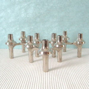 May include: A silver-toned metal modular candle holder featuring multiple interconnected cylindrical sockets with flared bases. The structure consists of several linked units arranged in a geometric formation, each designed to hold a single taper candle.