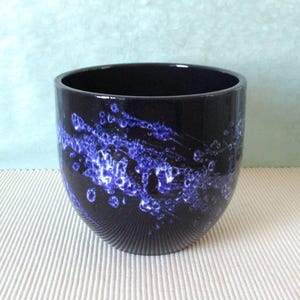 Op de afbeelding: Een witte keramische mok met een zwart handvat en de tekst "But First, Coffee" in een zwarte, handgeschreven lettertype. De mok staat op een wit oppervlak.