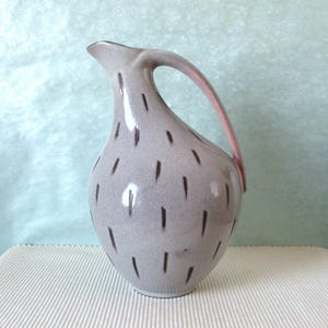 Könnte beinhalten: Eine weiße Keramik-Tasse mit schwarzem Henkel und dem Text "But First, Coffee" in fetter, schwarzer Schrift. Die Tasse steht vor einem verschwommenen Hintergrund, der eine gemütliche Umgebung suggeriert.