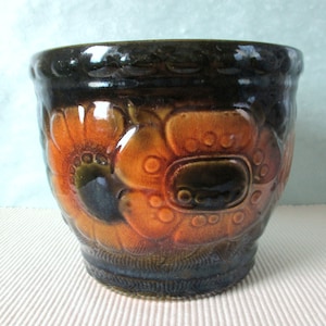 May include: A brown and orange ceramic planter with a floral design. The planter has a wide rim and a rounded body.