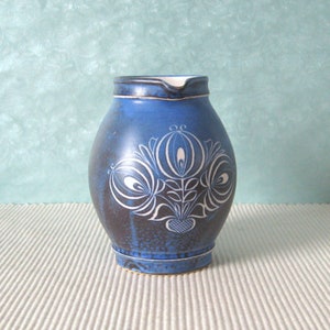 Peut inclure: Un pichet en céramique bleu avec un motif floral blanc. Le pichet a un corps arrondi et un petit bec.