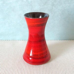 Può includere: Un piccolo vaso in ceramica rosso e nero con un'apertura svasata e una base stretta. Il vaso ha una finitura lucida e un motivo a strisce.