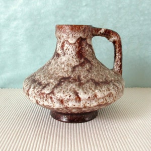 Könnte beinhalten: Eine braune und weiße Keramikvase mit einer strukturierten Oberfläche und einem Henkel. Die Vase hat einen breiten Boden und einen schmalen Hals.