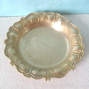 May include: A silver-toned metal dish with a scalloped edge and a decorative design. The dish is round and has a smooth, reflective surface.