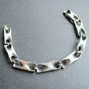 Puede incluir: Un brazalete de plata con un diseño geométrico único. Los eslabones están hechos de piezas planas y rectangulares con recortes, creando un aspecto moderno y minimalista.