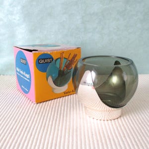 Op de afbeelding: Een vintage Quist Vario-Kugel glazen kom met een zilverkleurige voet. De kom heeft een rookgrijze kleur en staat naast de originele doos, met het Quist-logo en productinformatie.