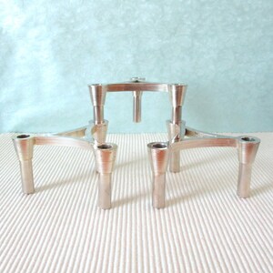 Peut inclure: Ensemble de bougeoirs argentés. Les bougeoirs présentent un design géométrique avec une plateforme centrale et trois pieds. Les bougeoirs sont en métal et présentent une texture nervurée sur la base et la coupelle.