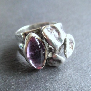 May include: A silver ring featuring a textured band and a large, oval purple gemstone. The ring has an unusual, organic design with additional silver detailing.