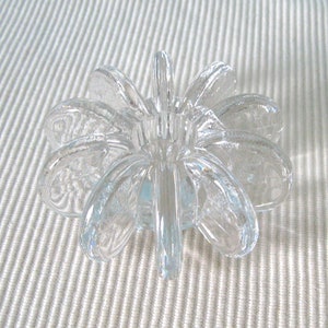 Puede incluir: Un portavelas de vidrio transparente con un diseño único en forma de flor. El portavelas tiene varios pétalos que se curvan hacia adentro para crear un espacio central para una vela.