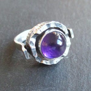 Op de afbeelding: Een zilveren ring met een getextureerde band en een ronde, paarse amethist edelsteen.