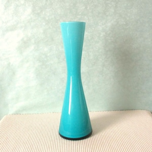 May include: A turquoise glass vase with a wide base and a narrow neck. The vase is made of smooth, glossy glass and has a gradient colour from light blue to dark blue.