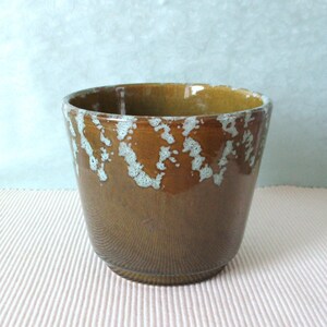 May include: A brown ceramic planter with a glossy finish. The rim features a white and light blue speckled design. The planter has a tapered shape and is suitable for indoor or outdoor use. The planter is approximately 15 cm tall.