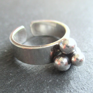 Puede incluir: Anillo ajustable plateado con un grupo de tres pequeñas cuentas redondas. El anillo tiene un diseño simple y moderno con una superficie ligeramente texturizada. El anillo está abierto en la parte superior, lo que permite ajustar la talla.