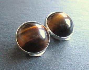 Puede incluir: Un par de pendientes de tono plateado con piedras redondas de ojo de tigre.