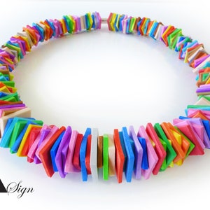 Op de afbeelding: Een kleurrijke ketting bestaande uit vierkante, platte kralen in verschillende kleuren, waaronder rood, oranje, geel, groen, blauw en paars. De kralen zijn aan elkaar geregen en vormen een cirkelvorm. De ketting wordt gepresenteerd tegen een witte achtergrond.