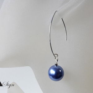 Può includere: Un singolo orecchino con un filo d'argento curvo e una perla blu rotonda e pendente. L'orecchino è mostrato su uno sfondo bianco, suggerendo un design di gioielli minimalista. La perla ha una finitura lucida.