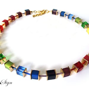Puede incluir: Un collar de colores arcoíris con cuentas cuadradas conectadas por eslabones de cadena dorados. El collar está hecho de vidrio y metal.