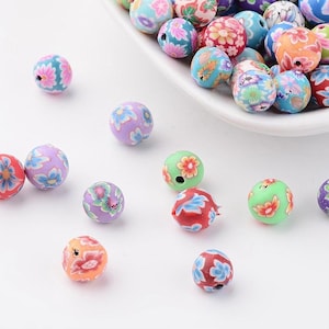 Könnte beinhalten: Sortiment an bunten runden Perlen mit Blumenmustern. Die Perlen sind aus Polymer Clay gefertigt und haben ein Loch zum Auf fädeln.