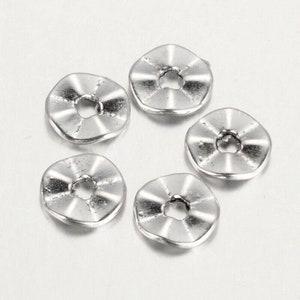 Può includere: Cinque perline distanziatrici in metallo argentato con bordo a festoni e un foro rotondo al centro.