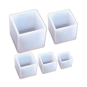 Könnte beinhalten: Satz mit vier weißen quadratischen Silikonformen in verschiedenen Größen. Die Formen sind aus flexiblem Silikon und eignen sich perfekt für die Herstellung kleiner Handarbeiten wie Seife, Harz oder Kerzen.