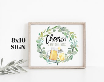 May include: A white 8x10 inch sign with a green leafy wreath surrounding a beer mug and a baby bottle. The text reads "Cheers! A baby is brewing."