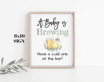 May include: A white 8x10 inch sign with a brown wood frame. The sign says "A Baby is Brewing" with a beer mug and a baby bottle. The text below says "Have a cold one at the bar!"