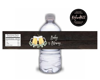 May include: Water bottle label with a rustic wood background. The label features a nutrition facts table with the text "Baby is Brewing". Two cartoon beer mugs with a green leafy design are on the label.