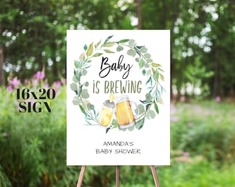 May include: A white 16x20 inch sign with a green watercolor wreath and the text "Baby is Brewing".  There are two illustrations of bottles, one with a baby bottle and one with a beer bottle.  The text "Amanda's Baby Shower" is at the bottom of the sign.