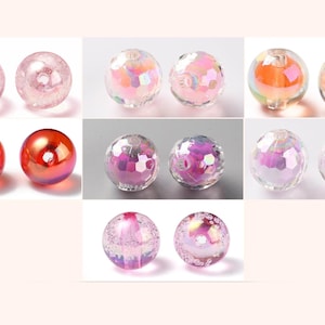 Könnte beinhalten: Eine Sammlung runder Perlen in verschiedenen Ausführungen, darunter durchscheinendes Rosa mit inneren Rissstrukturen, facettiertes irisierendes Klarglas, glattes metallisches Rot und violett getönte Kugeln, alle mit zentralen Fädellöchern.