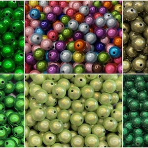 Könnte beinhalten: Eine Sammlung runder Perlen in verschiedenen Farben, darunter Grün, Mehrfarbig, Gold und Hellgrün. Die Perlen haben eine glänzende Oberfläche und ein Loch zum Auffädeln. Diese Perlen eignen sich für die Schmuckherstellung und Bastelarbeiten.