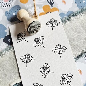 Könnte beinhalten: Eine weiße Karte mit einem schwarzen und weißen Stempeldesign einer Gänseblümchen. Die Karte liegt auf einem Stoffhintergrund mit einem Blumenmuster.