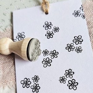 Könnte beinhalten: Ein Stempel aus Holz mit einem Blumenmuster, der verwendet wird, um mehrere Blumenabdrücke auf einer weißen Karte zu erstellen. Die Karte enthält auch den Text "www.stempeldreams.de".