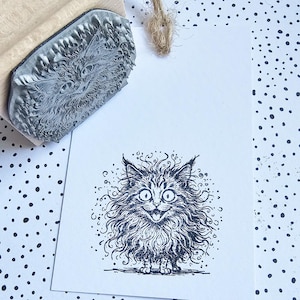 Könnte beinhalten: Ein Gummistempel mit einem detaillierten Katzengesicht-Design. Der Stempel ist auf ein weißes Etikett gedrückt und erzeugt eine Schwarz-Weiß-Illustration einer flauschigen Katze mit großen Augen und offenem Mund. Der Stempel besteht aus Holz und Gummi.