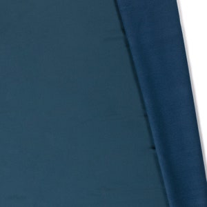 May include: Two pieces of fabric, one a dark teal blue and the other a slightly darker blue, are folded over each other. The fabric is smooth and has a slight sheen.