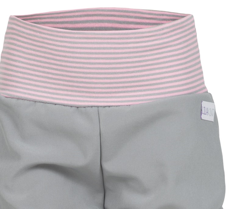 May include: Gray shorts with a pink and gray striped waistband. The shorts have a small white label with the text "SLACKZ" on the right side.