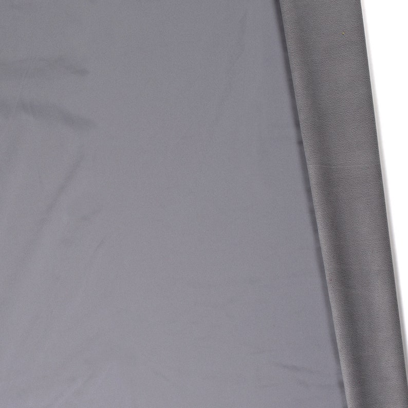 May include: A close-up of a piece of gray fabric. The fabric is smooth and has a slight sheen. The fabric is folded over on itself, revealing a darker gray underside.