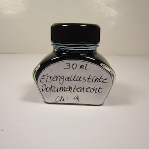 Könnte beinhalten: Kleine, klare Glas-Tintenflasche mit schwarzem Deckel, gefüllt mit dunkelblauer Tinte. Auf dem Etikett steht "30 ml Eisengallustinte Dokumentenecht Ch: 9".
