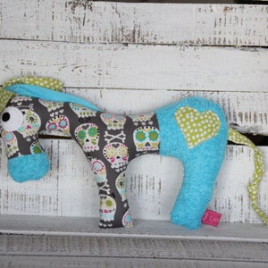 以下が含まれることがあります： 緑と白のドット柄のハートが側面に付いた、青と灰色のぬいぐるみ馬。馬の体にはドクロとクロスボーンの模様があります。