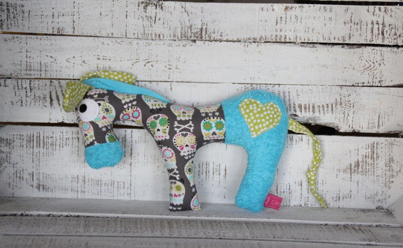 以下が含まれることがあります： 緑と白のドット柄のハートが側面に付いた、青と灰色のぬいぐるみ馬。馬の体にはドクロとクロスボーンの模様があります。