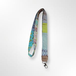 Könnte beinhalten: Ein farbenfrohes Lanyard mit Patchwork-Design in Blau, Grün, Gelb und Rosa. Das Lanyard hat einen silbernen Drehverschluss.