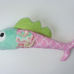 Könnte beinhalten: Ein Plüschfisch mit einer grünen Flosse, rosa Schuppen und einem blau-rosa Paisley-Muster an der Seite. Der Fisch hat ein großes, schwarzes Auge und einen rosa Schwanz.