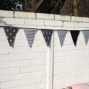 Może przedstawiać: Czarno-biała girlanda z różnymi wzorami, w tym paski, gwiazdki i kształty geometryczne. Girlanda jest zawieszona na białej ceglanej ścianie.