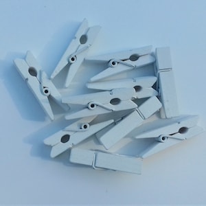 Può includere: Un gruppo di dieci mollette di legno bianche. Le mollette sono disposte in un mucchio, con alcune sovrapposte.